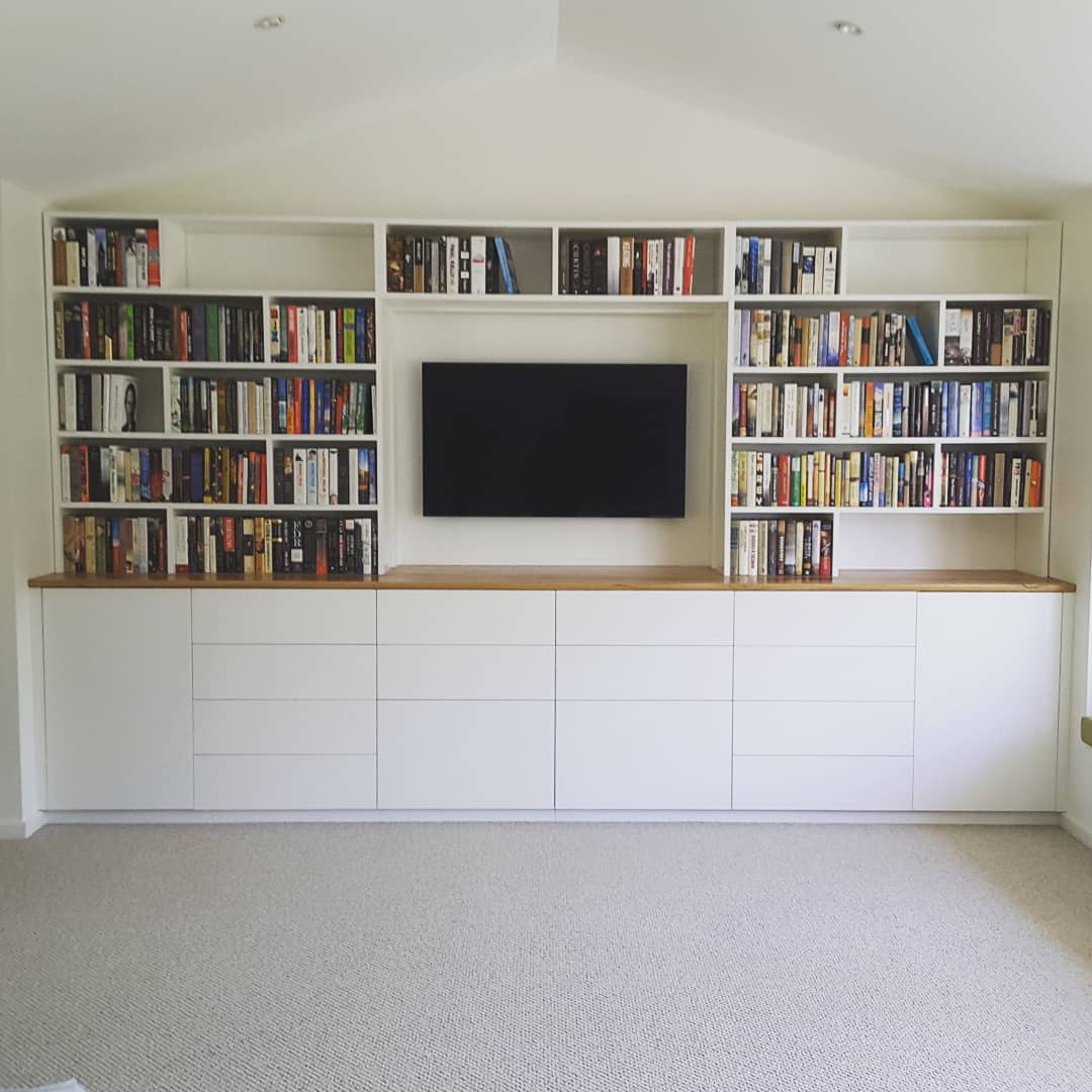Bookshelf filled with books, with TV in centre and white drawers at bottom
